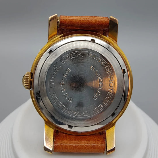 Photo d'une montre vintage Regor Precision 1950, mouvement manuel, cadran crème/argenté, sur fond uni.